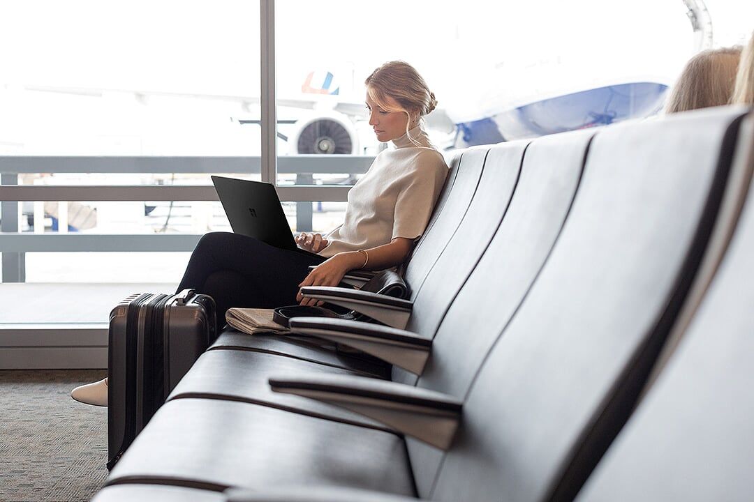 Eine Frau sitzt in der Wartehalle eines Flughafens und arbeitet mit ihrem Surface Laptop ortsunabhängig und flexibel