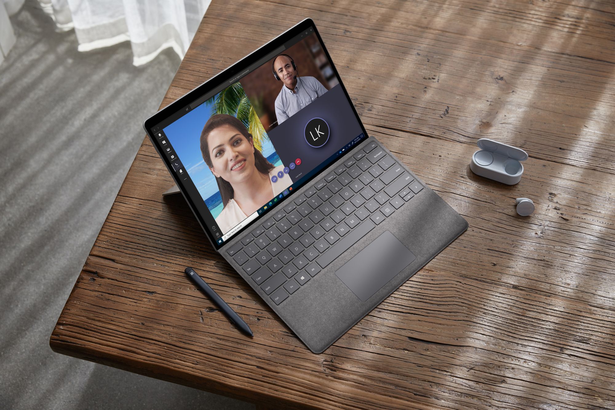 Das Surface Pro X steht auf einem Tisch mit Signature Keyboard in Platin im Laptop-Modus, links vom Surface sind der Slim Pen und rechts die Surface Earbuds platziert