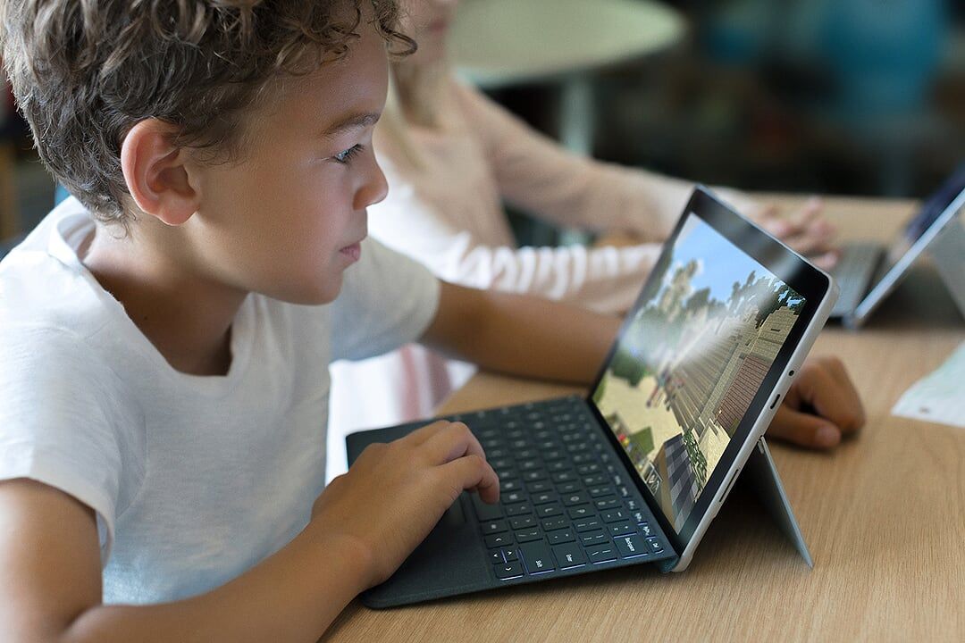 Ein Junge sitzt an einem Tisch und spielt etwas auf dem Surface Go inklusive Type Cover