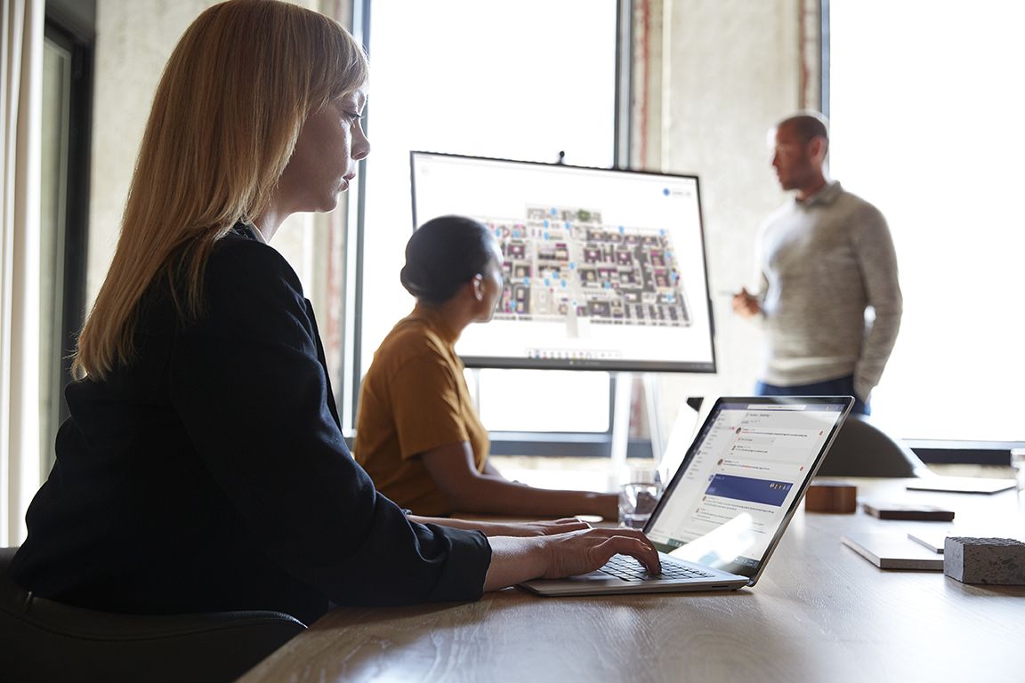 I et mødelokale arbejder tre personer sammen med Surface Hub og Surface Laptops