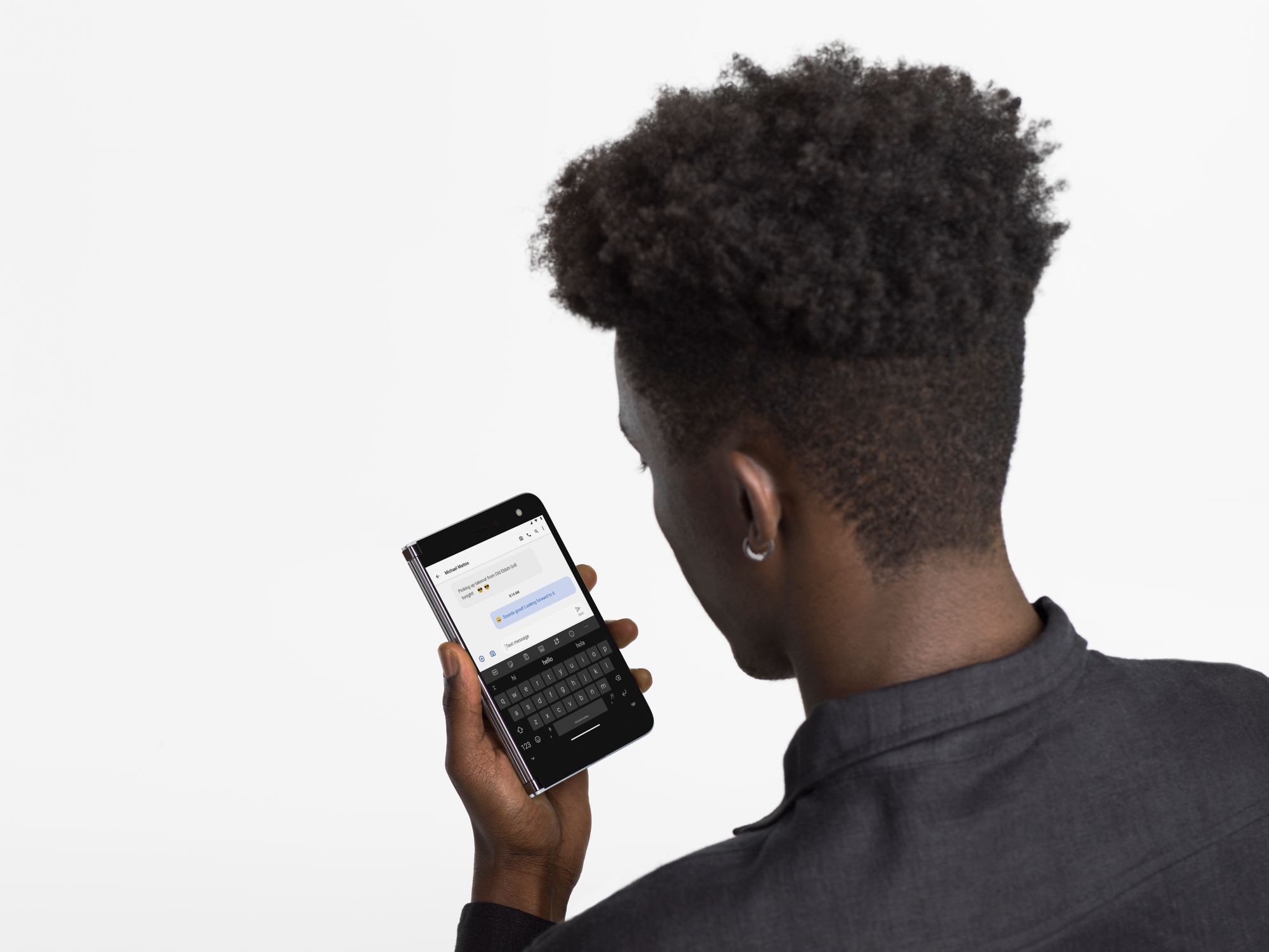 En mand holder sin Surface Duo i hånden i telefontilstand og ser på skærmen med et åbent chatvindue
